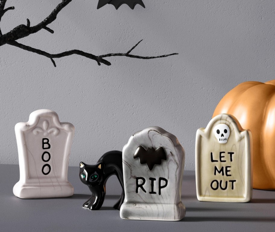 a ceramic cat figurine shown with 3 tombstone figurines on a mantle