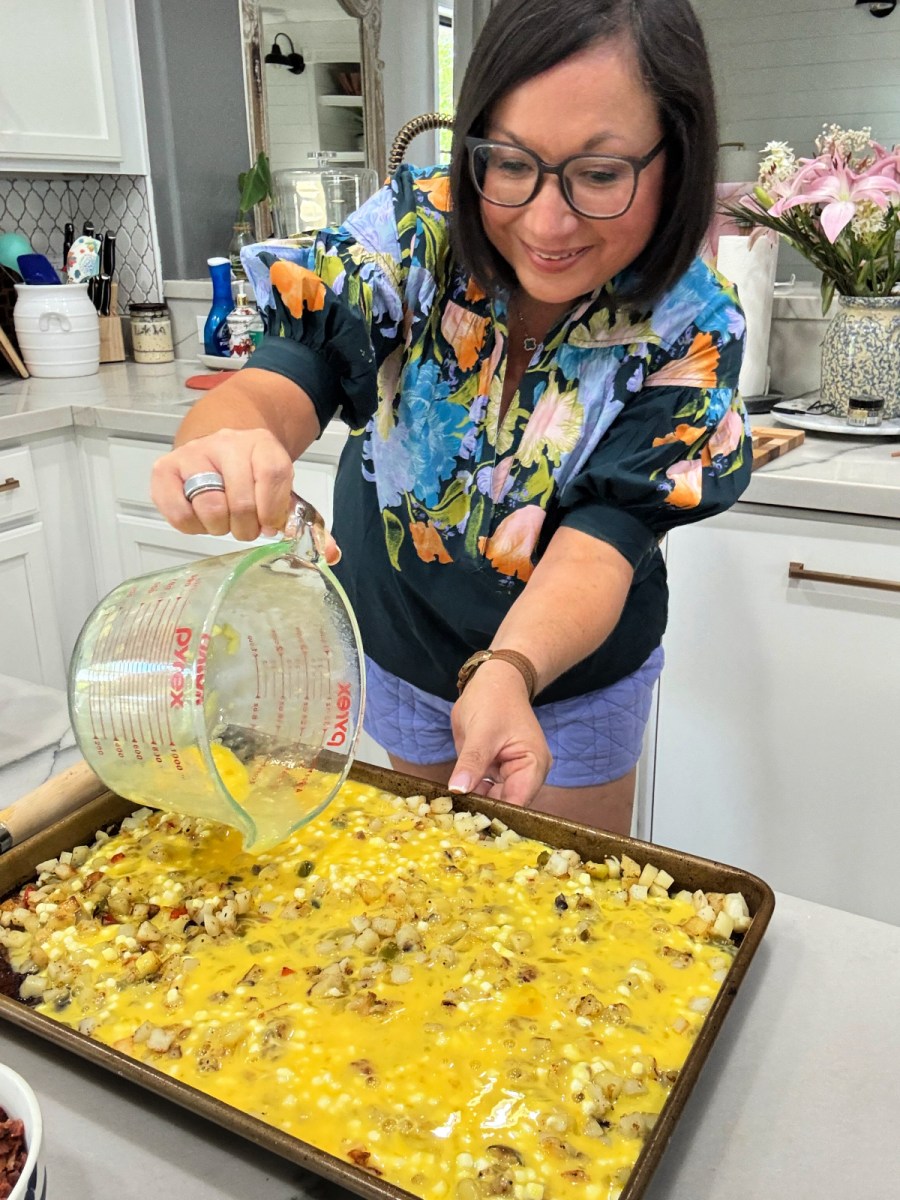 woman pouring eggs onto sheet pan with cooked potatoes 