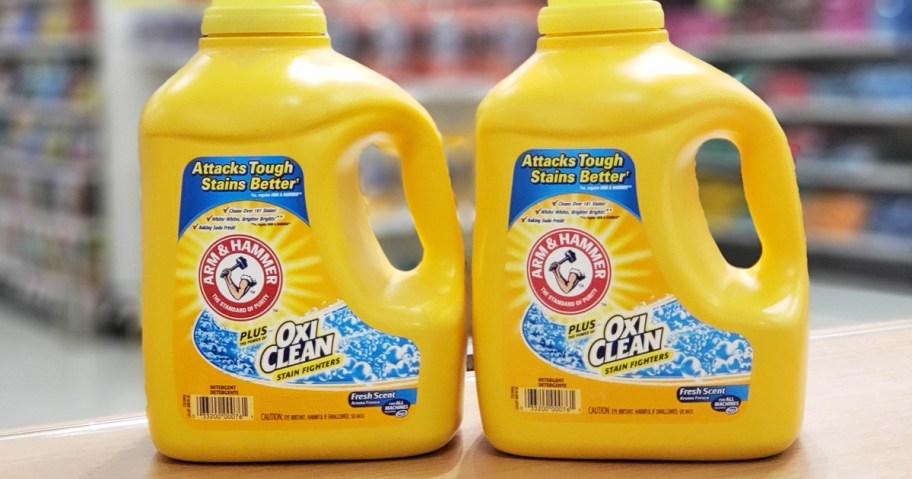 two large yellow bottles of Arm & Hammer Plus OxiClean Laundry Detergent on wood shelf