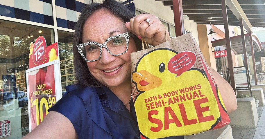 woman holding up a Bath & Body Works Semi-Annual Sale outside of store