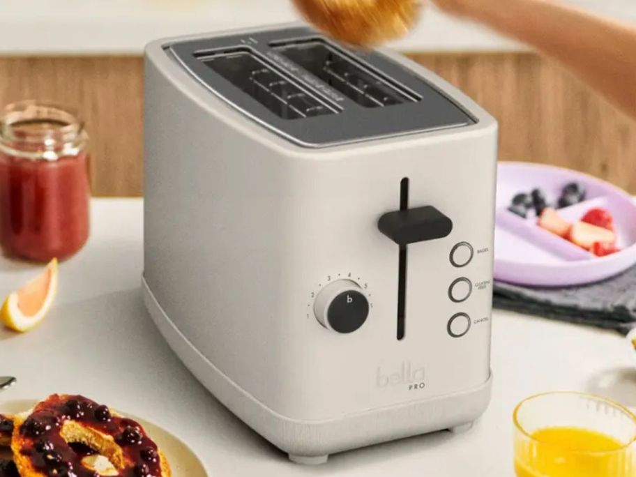An off-white toaster on a table surrounded by breakfast food