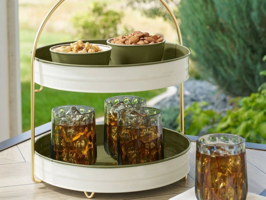 a circular 2-tiered green and white tray with drinks and snacks on it 