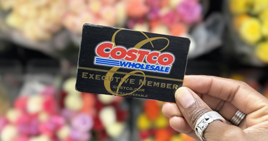 hand holding up Costco executive membership card in front of flowers
