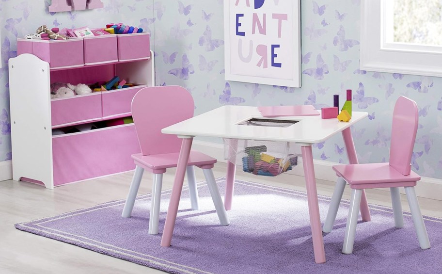 pink and white kids table with two matching chairs and toy storage bins in playroom