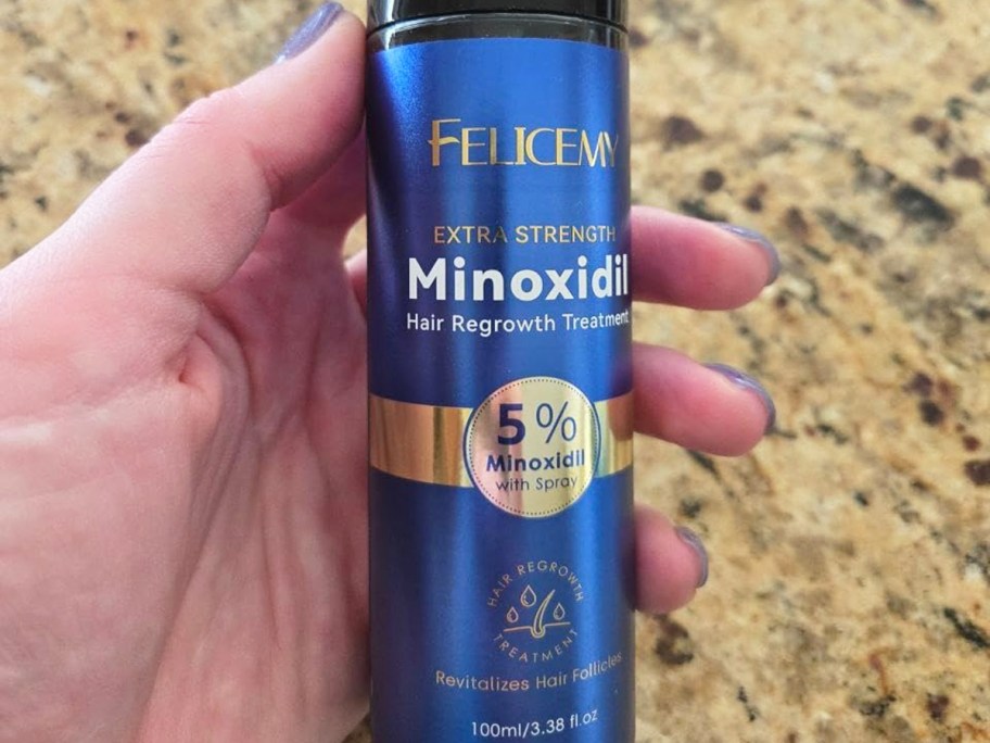 hand holding a blue can of Felicemy Minoxidil Hair Growth Treatment spray