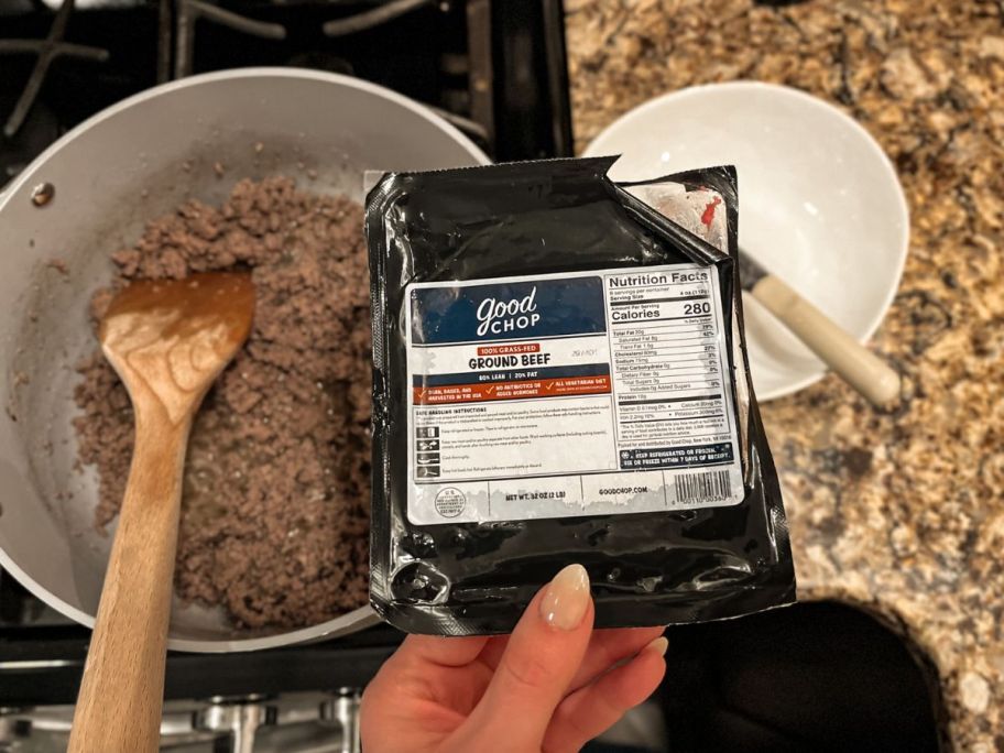 hand holding a packet of ground beef in front of a pan with ground beef inside