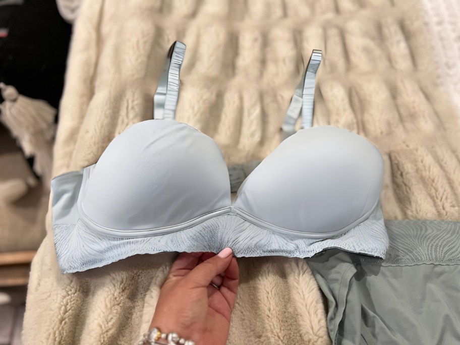 woman's hand reaching for a bra laying on a bed