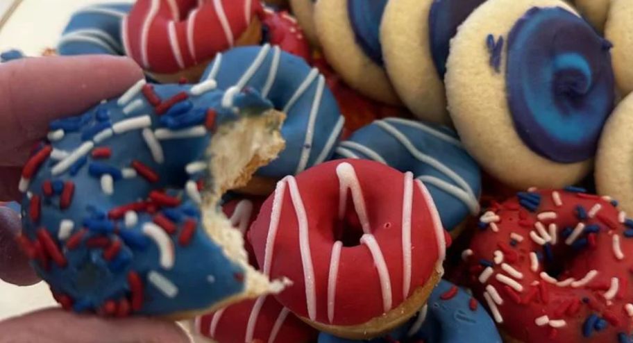 hand holding mini donut with a tray filled with donuts behind it 