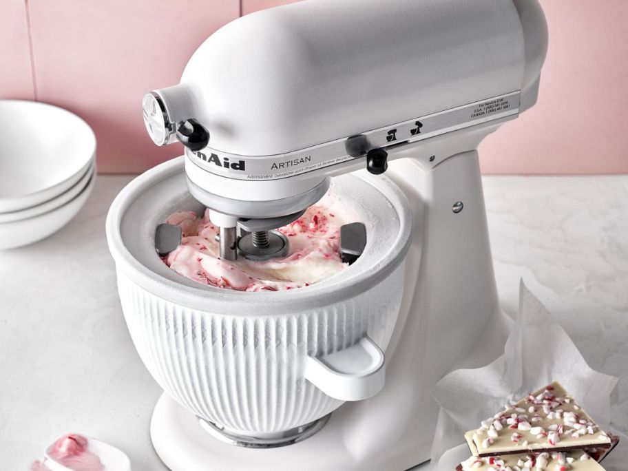 White kitchen aid with ice cream attachement making peppermint bark ice cream on a table with a spoon and bark next to it 