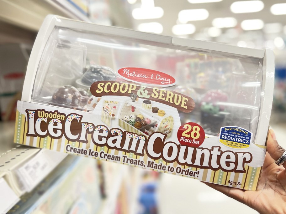 hand grabbing Melissa & Doug Wooden Scoop & Serve Ice Cream Counter set from store shelf