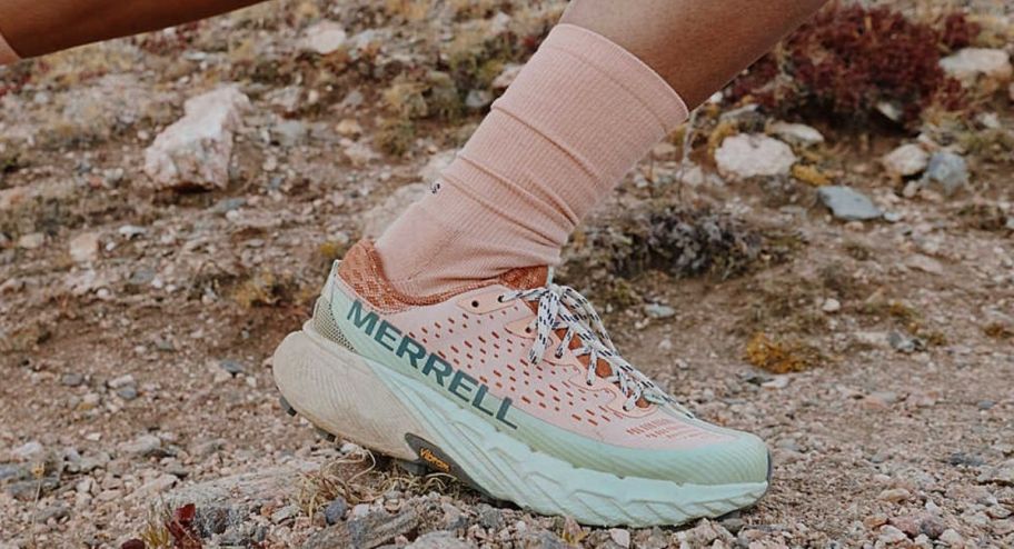person wearing Merrell shoes in pink and green on gravel getting ready to run with pink socks