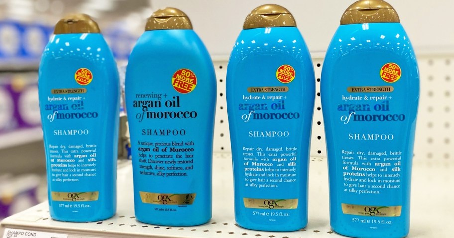 four blue bottles of OGX argan oil shampoo on store shelf