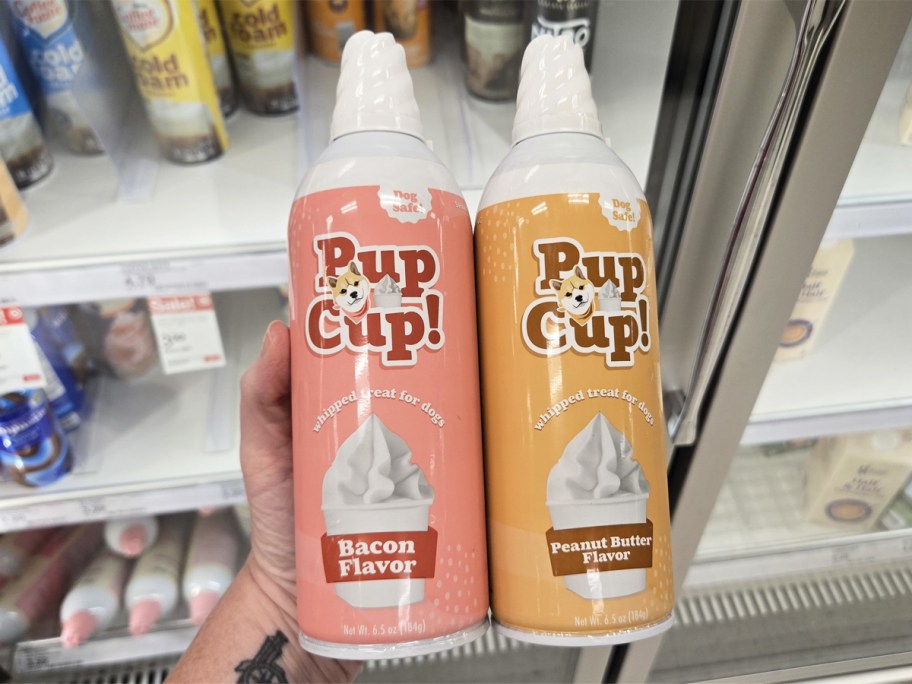 hand holding two cans of pupcup whipped cream in store