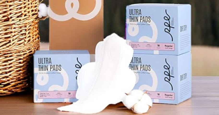 3 boxes of RPE Life Organic Pads with an open pad next to a raw cotton blossom