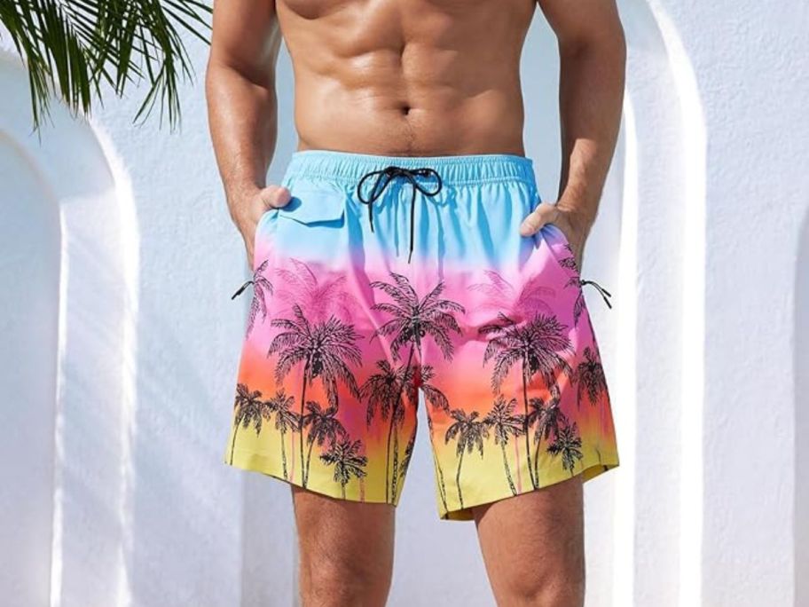 A man wearing a pair of swim trunks with palm trees on it 