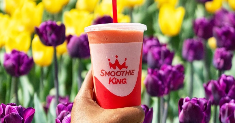 hand holding up a Smoothie King smoothie with field of purple and yellow tuplips in background