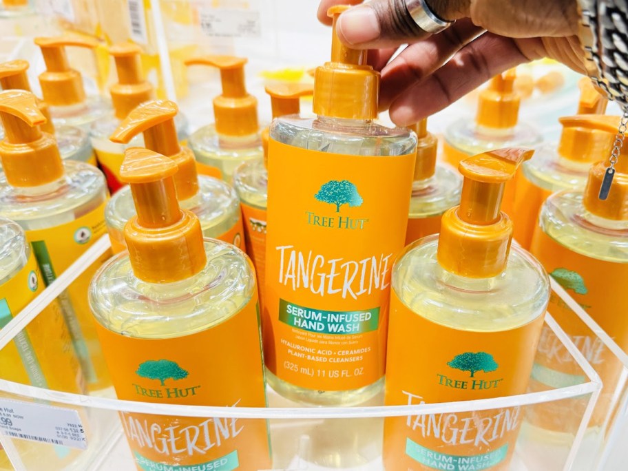 hand grabbing a bottle of Tree Hut Tangerine Serum Infused Hand Wash