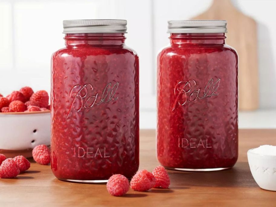 two Ball 32oz Glass Regular Mouth Rose Vintage Mason Jars with raspberry jam in them and raspberries around them on counter