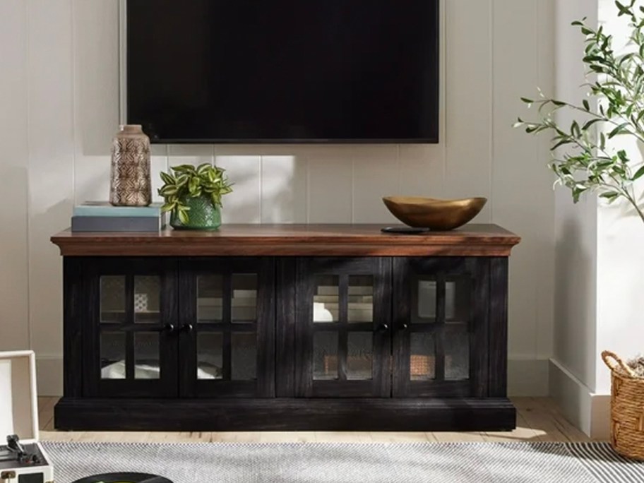 black tv stand with flowers and bowls on top and tv hanging above it 