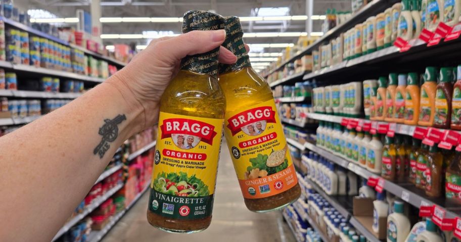hand holding two bottles of Bragg Organic Salad Dressing & Marinade in store