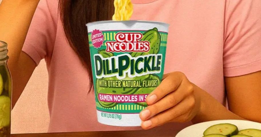 person eating nissin ramen cup noodles in dill pickle flavor