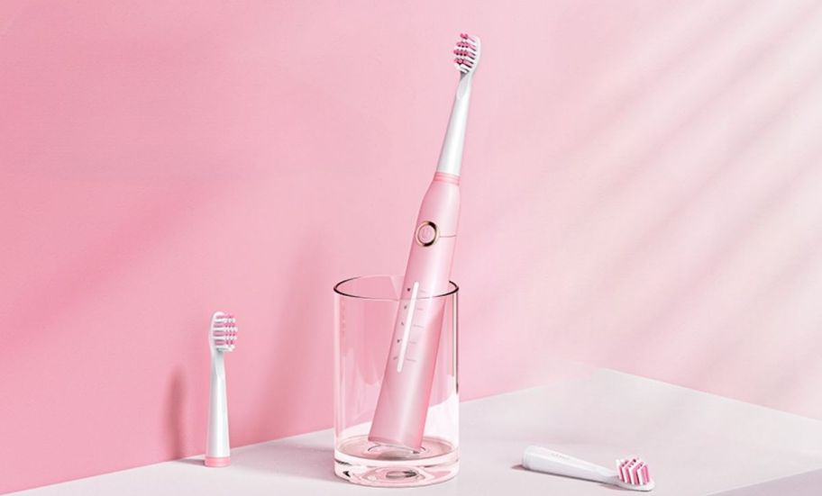 a pink electric toothbrush in a clear glass cup shown with 2 spare brush heads