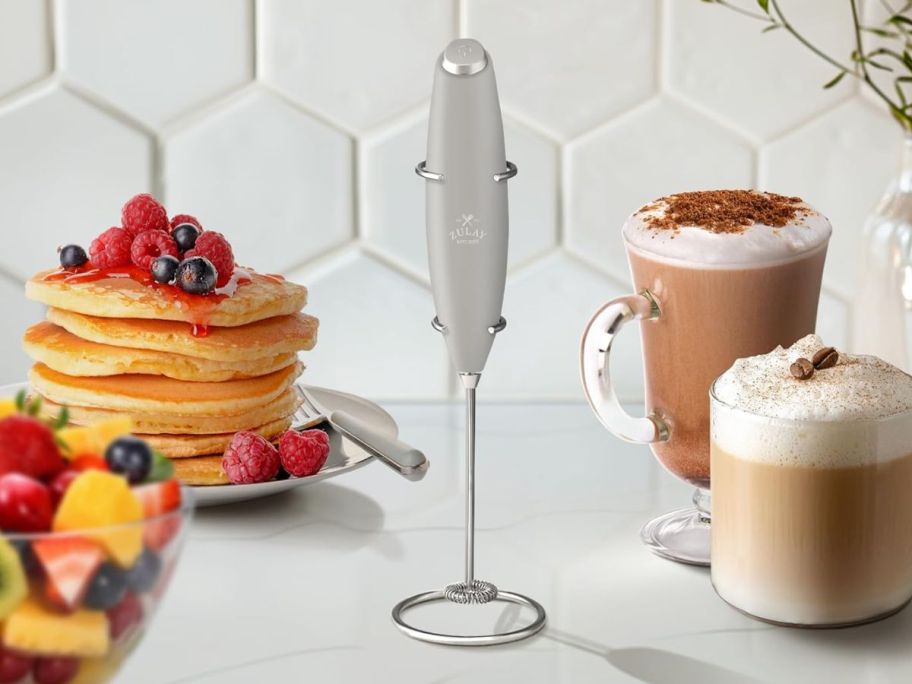 silver milk frother wand on counter in the middle of drinks and food