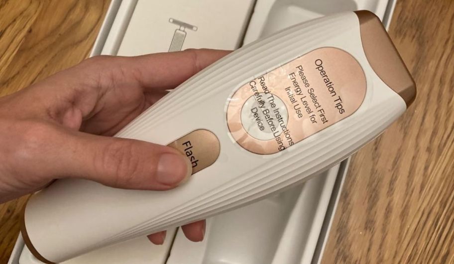 a womans hand holding a white and pink laser hair remover