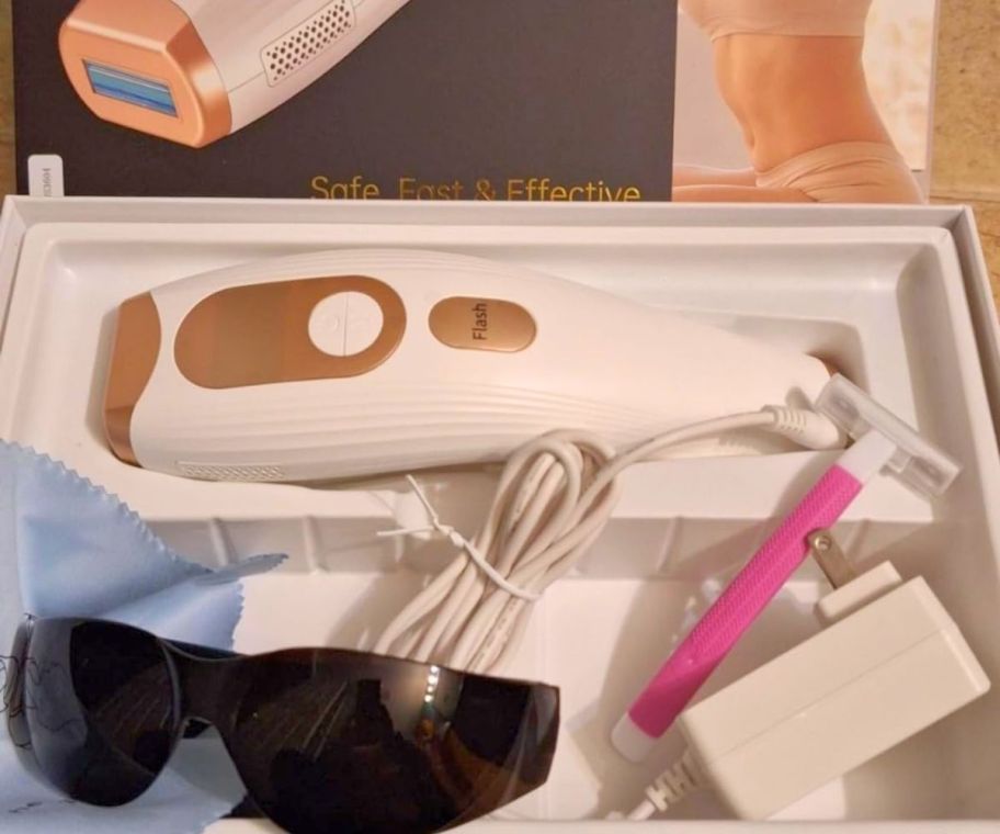 a white and pink laser hair remover shown with safety razor, sunglasses and power cord.