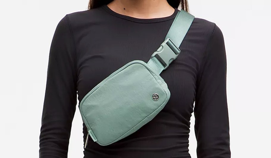 woman in a black long sleeve top with a green belt bag across her chest