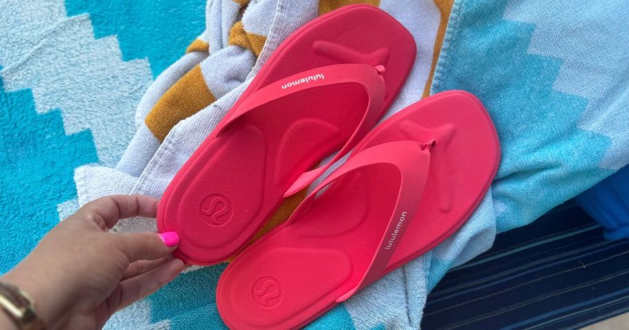 Hean touching a pair of pink lululemon Flip Flops on a beach towel