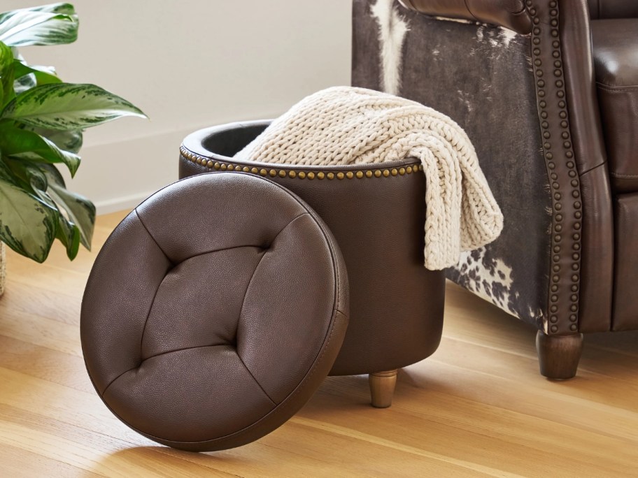 a brown faux leather storage ottoman open with a blanket partly in it
