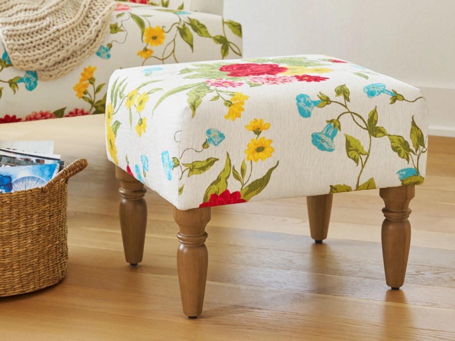 a floral fabric ottoman with wood legs in a living room 