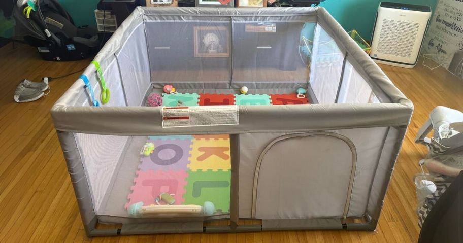 grey baby playpen with mat and toys inside