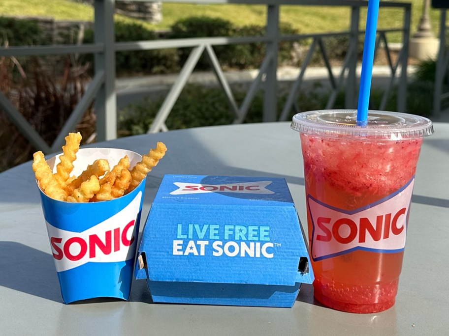 fries, a burger carton, and a red slushie from Sonic on a table outdoors