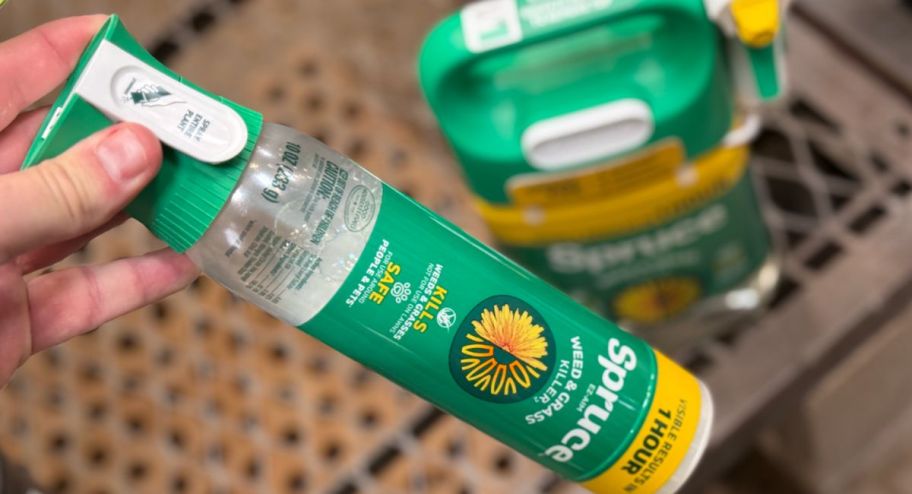hand holding a spruce weed killer with a big bottle behind it
