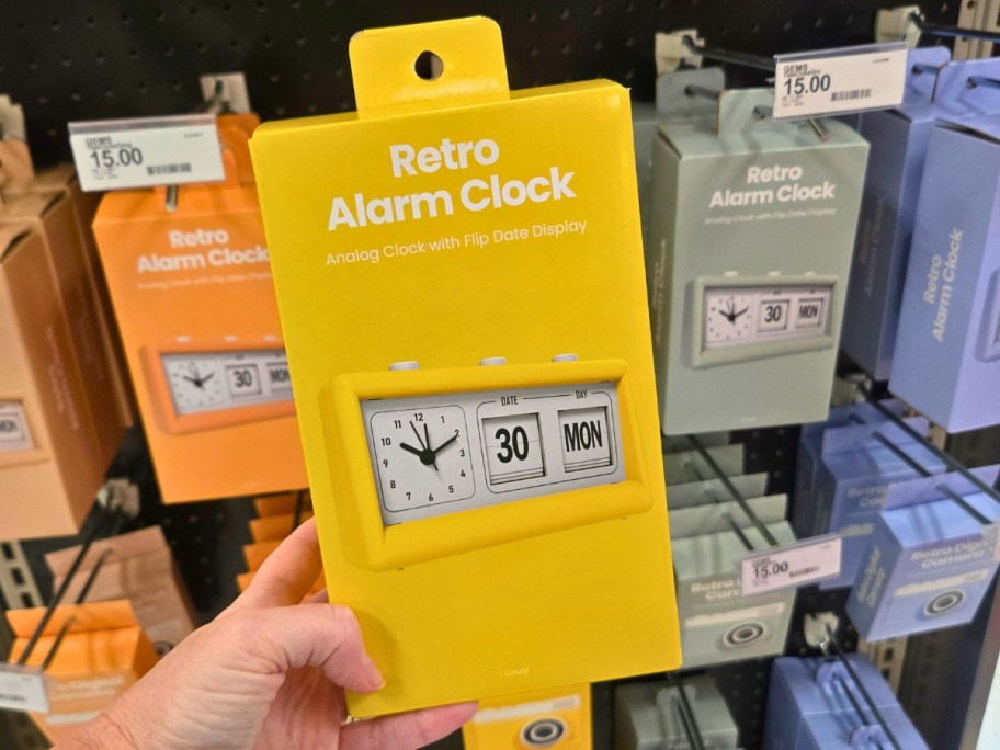 hand holding a box with a retro alarm clock in it, more on a store shelf behind it