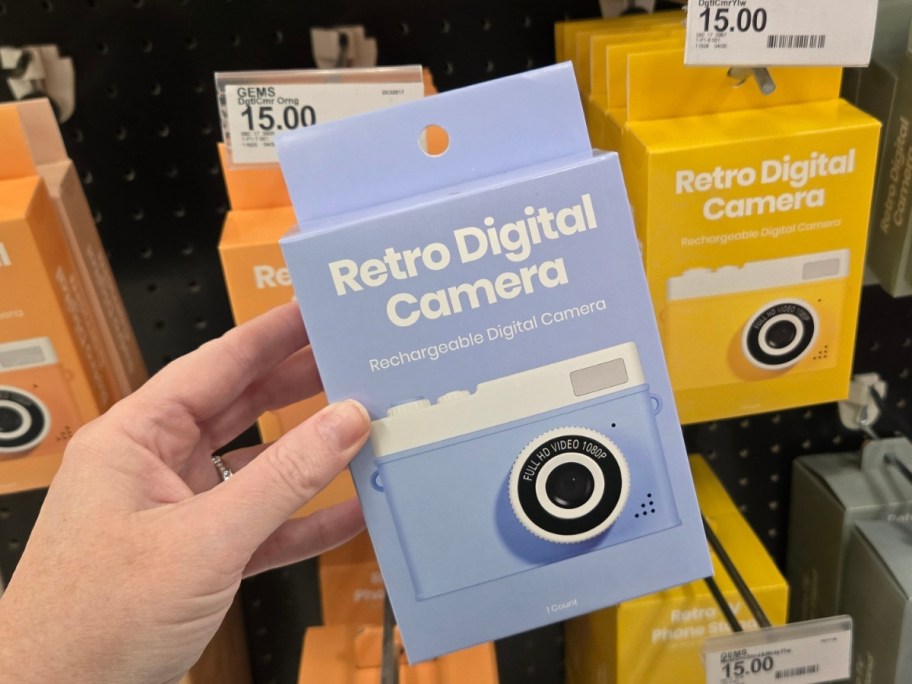 hand holding a box with a retro digital camera in it, more on a store shelf behind it 