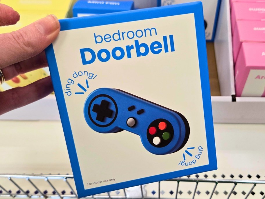 hand holding a box with a bedroom doorbell shaped like a game controller, more on a store shelf behind it