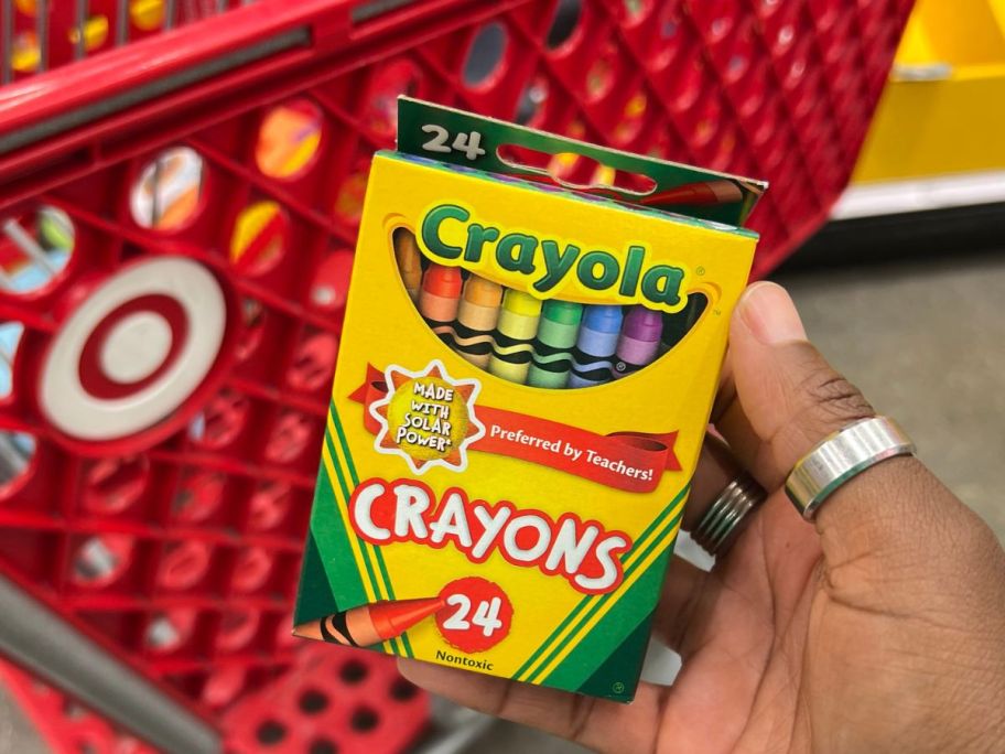 hand holding a box of Crayola Crayons in front of a target shopping cart