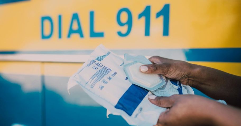 Hands holding medical supplies in front of writing that says Dial 911 on an ambulance