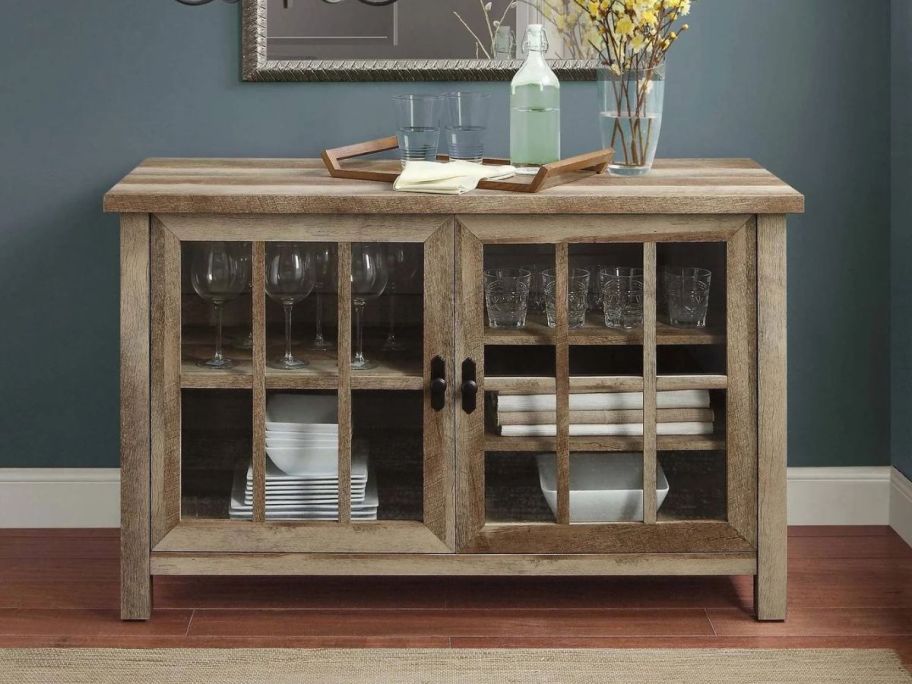 A Better Homes & Gardens Oxford Square TV Stand with plates and glassware items in and on it