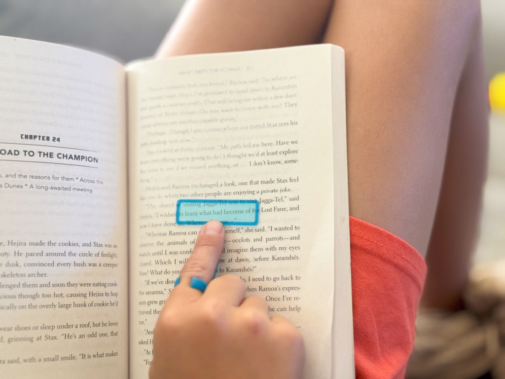 Little boy using blue plastic reading strip to read paperback book