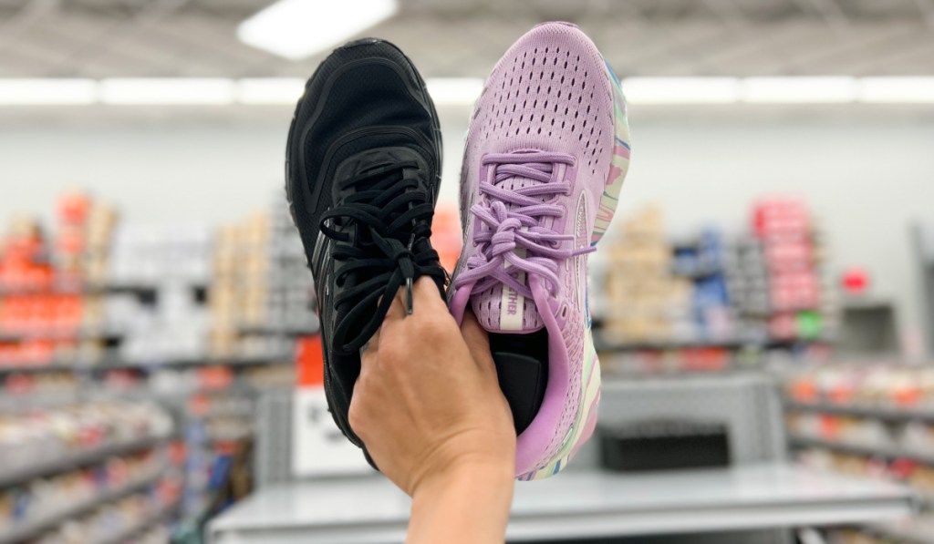 Woman holding a pair of black and purple Brooks running shoes inside store