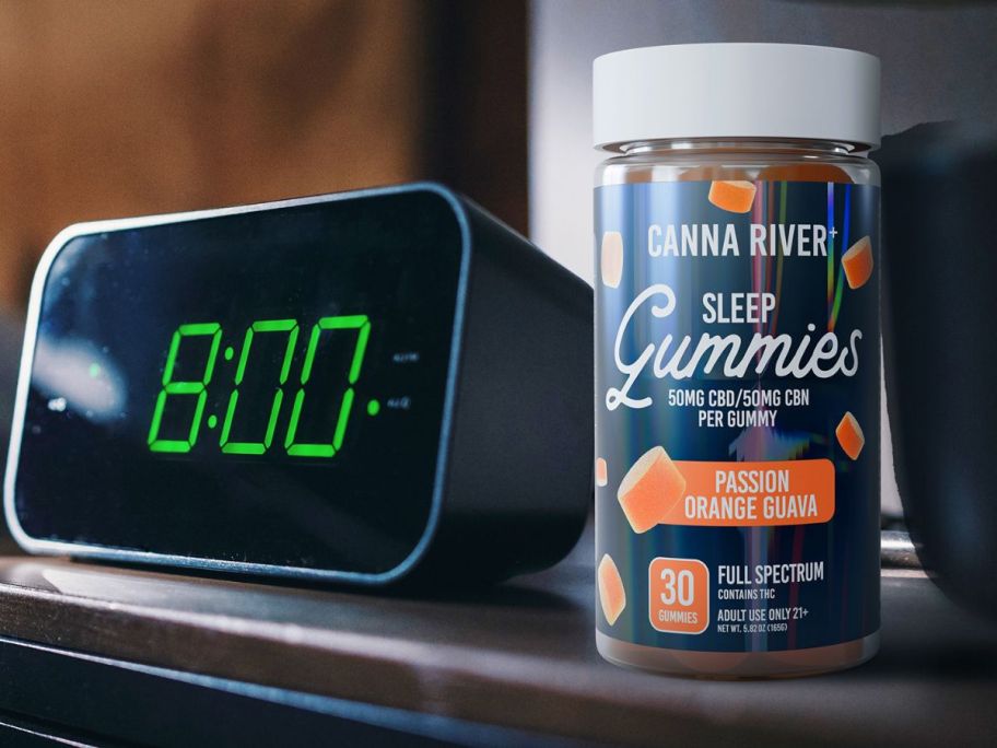 A bottle of canna River sleep gummies next to an alarm clock