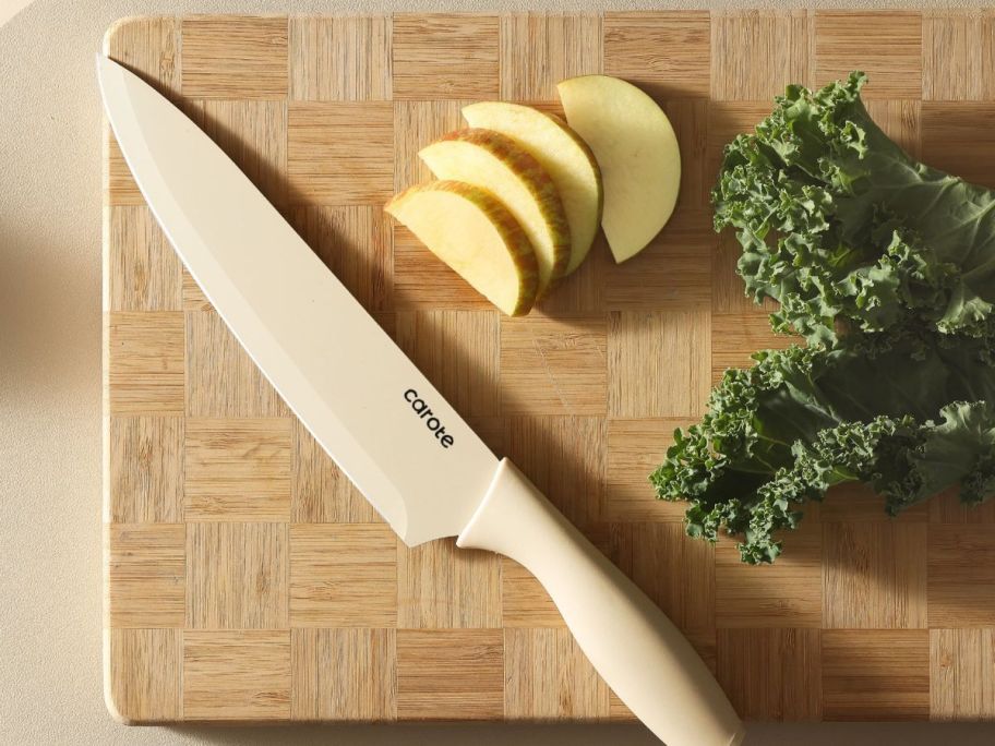 A Carote Knife on a wooden cutting board with slices of apple next to it and some greens