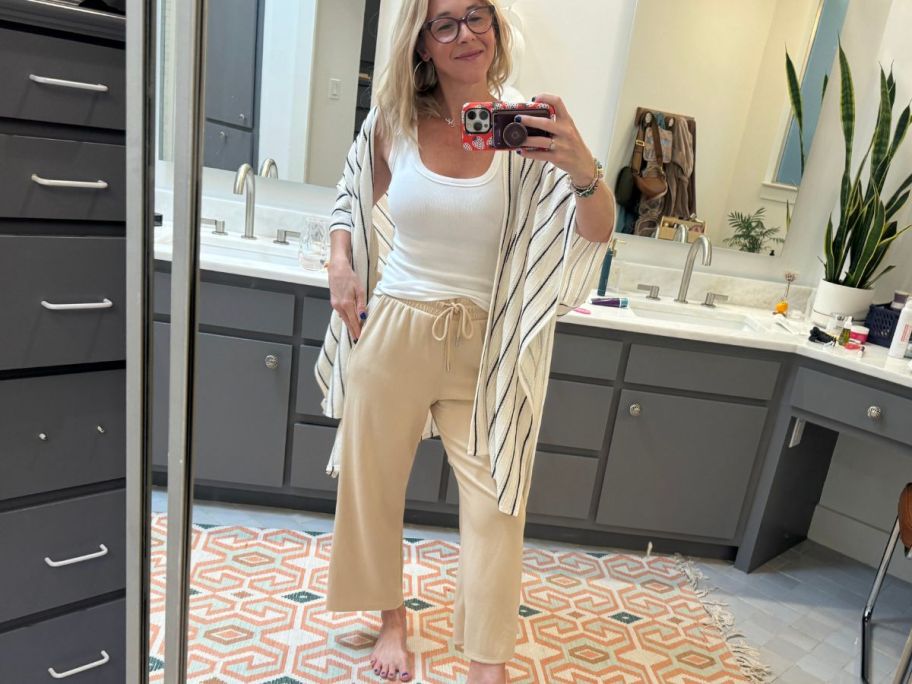 A woman wearing Scoop Women's ScubaKnit sweatpants, a white tank top, and duster in a bathroom