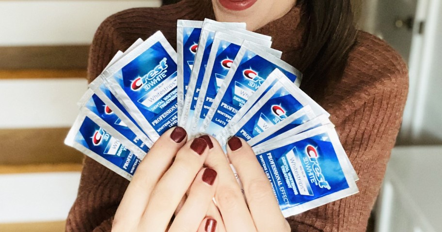 woman holding up multiple packs of Crest 3D Whitestrips