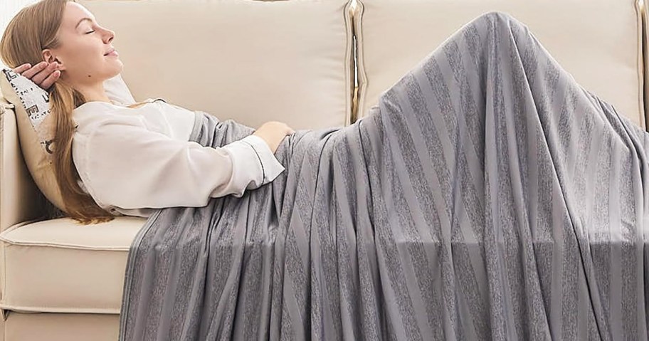 woman sleeping on couch under a grey striped blanket