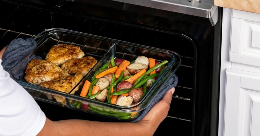 person holding ello divided 9x13 baking dish with baked chicken and vegetables